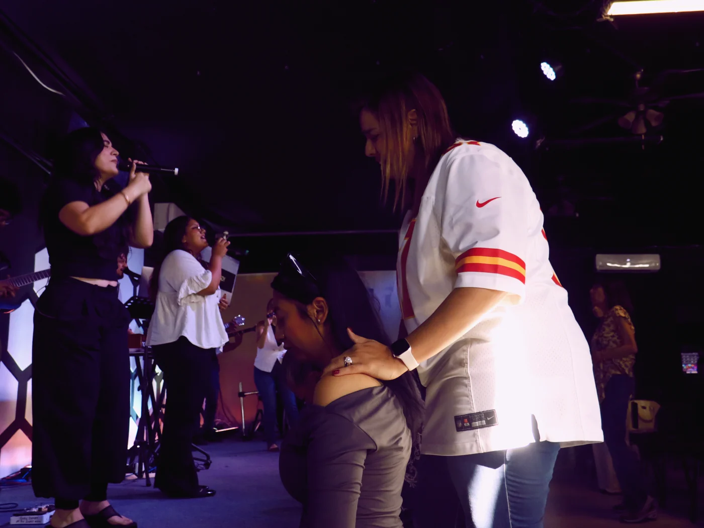 Equipo de alabanza cantando en el escenario de Hope City mientras una mujer ora por otra al frente, en García, N.L.